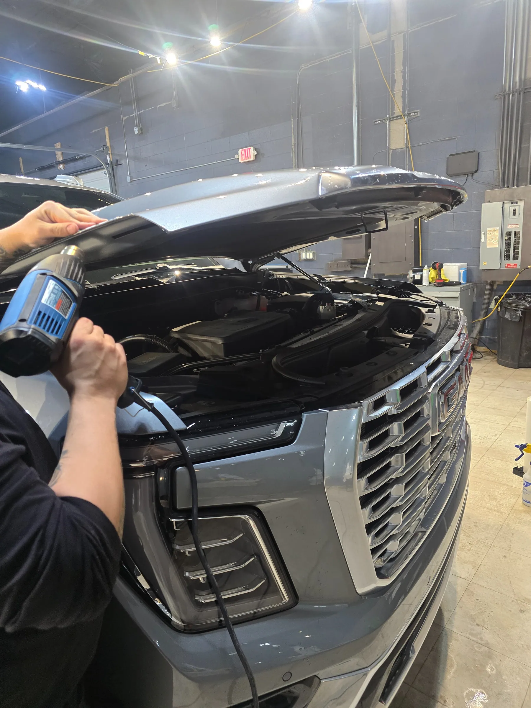 Installer using a heat gun along the edge of an open Cadillac hood