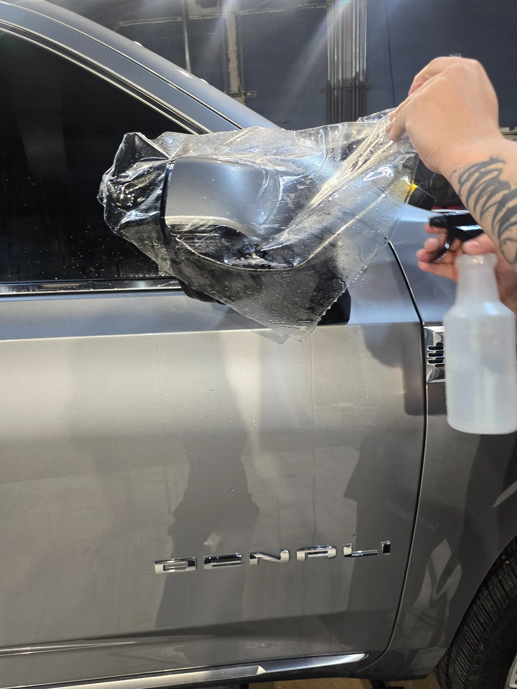 Installer fitting clear film around a silver vehicle side mirror